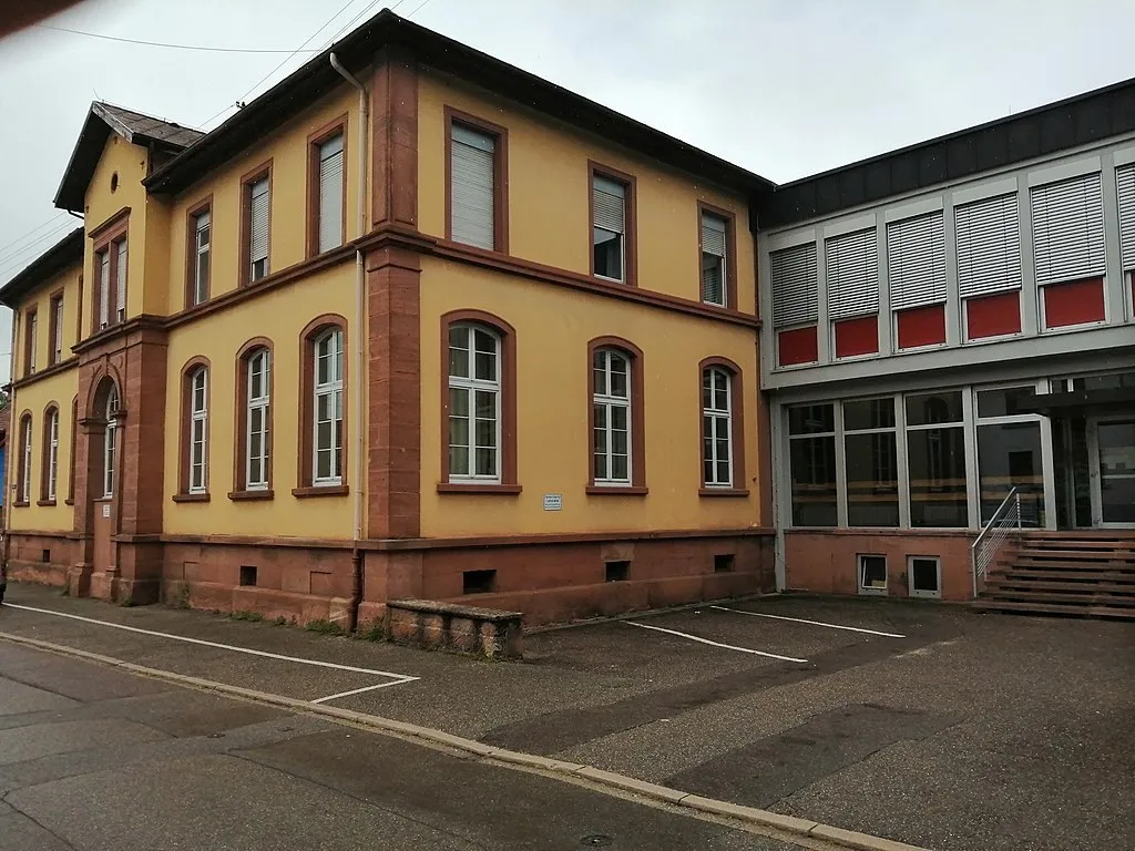 Der Altbau der Grundschule Sulz von 1900: gelbe Fassade mit rotem Sandstein, rechts daneben der neuere Trakt mit großen Fenstern.
